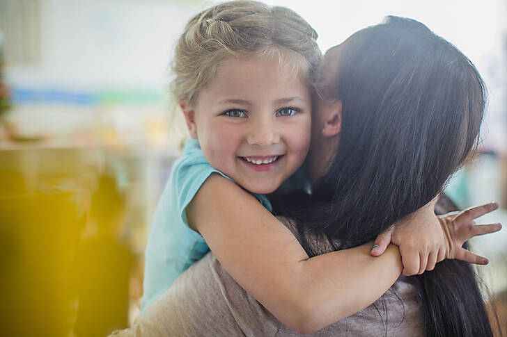 Portrait of smiling girl in kindergarten hugging pre-school teacher
